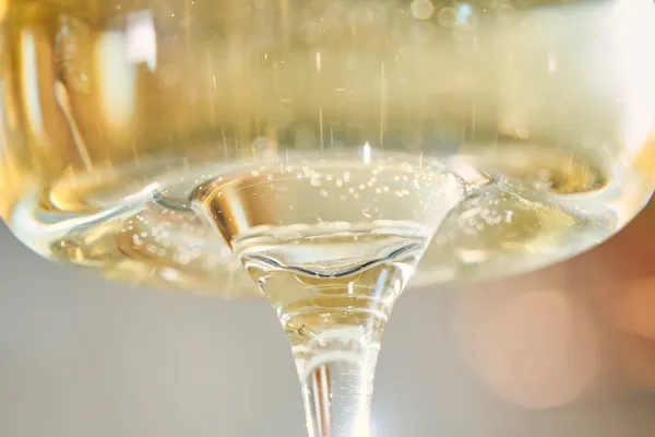 Nahaufnahme eines Glases mit prickelndem Weißwein – Blick durch den Stiel mit sichtbaren aufsteigenden Kohlensäurebläschen