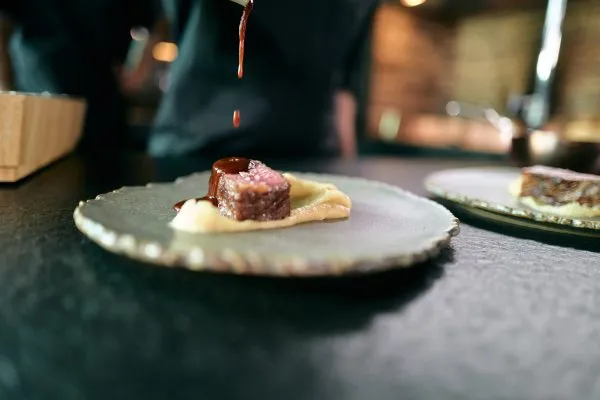 Ein kunstvoll angerichtetes Stück gegrilltes Fleisch auf cremigem Püree, verfeinert mit einer langsam herabtropfenden, dunklen Sauce – moderne südamerikanische Feinschmeckerküche