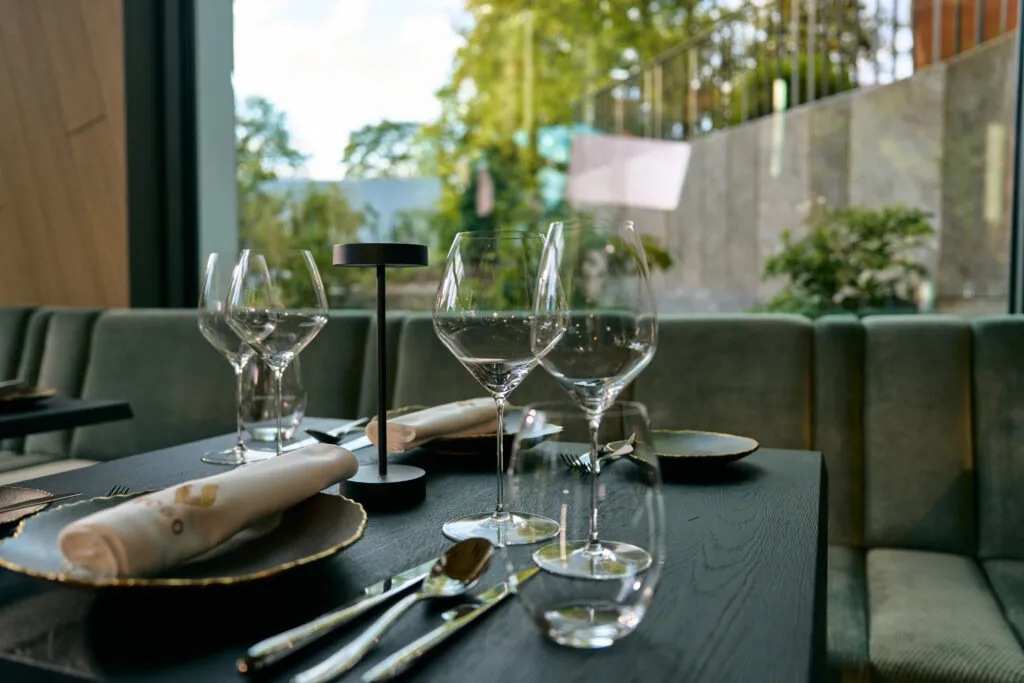 Elegant gedeckter Tisch im Fine Dining Restaurant des Alea Resorts mit modernen Weingläsern, Stoffservietten und Blick ins Grüne durch eine große Fensterfront